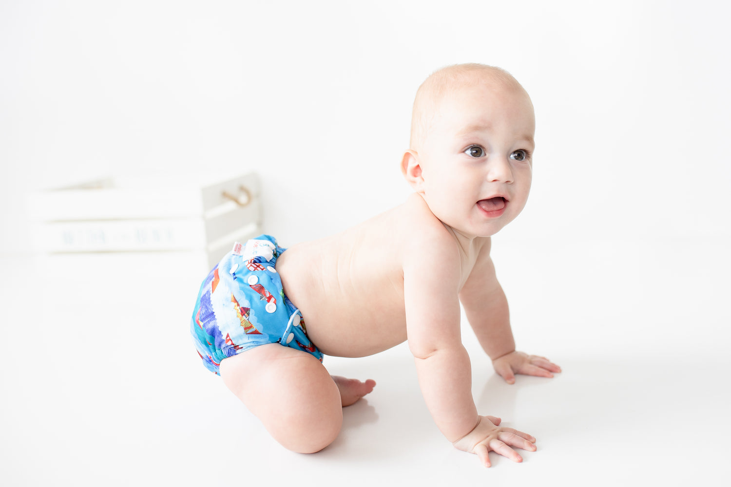 A crawling happy baby wearing a Bubblebubs Candie cloth nappy. He looks like he is still learning to crawl as he stumbles wearing his blue reusable nappy.