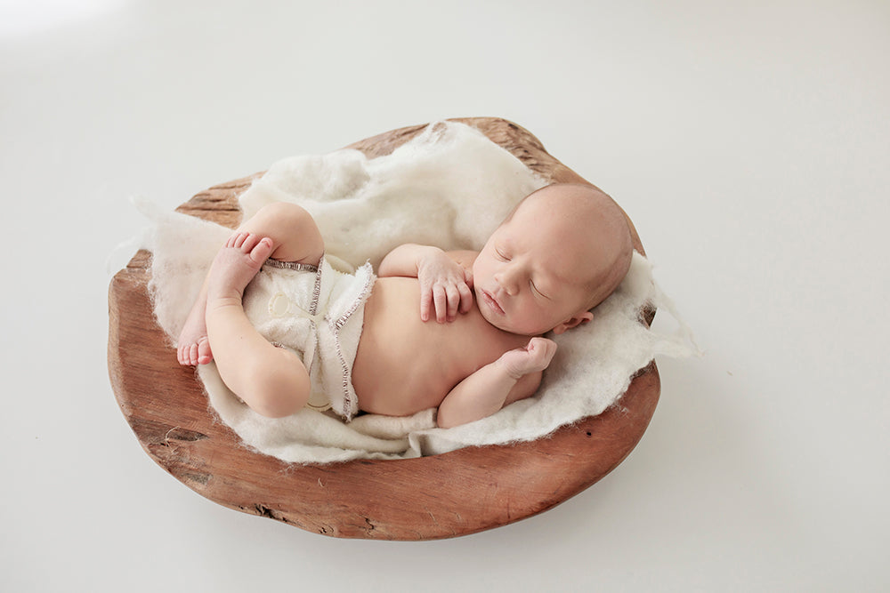 Sleeping baby waring a Bubblebubs Bambam cloth nappy on a small cloth in a round log.
