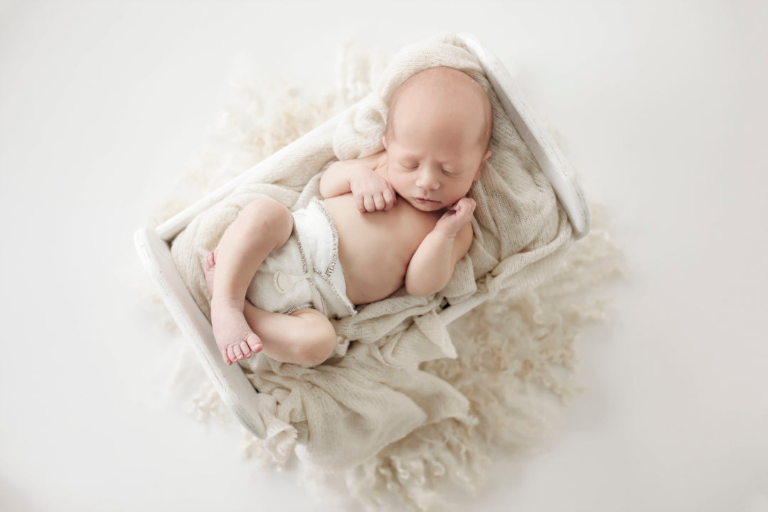A very small baby just 2kg sleeping in a box on lambswool waring a Bubblebubs Bambam cloth nappy done up with a snappi.