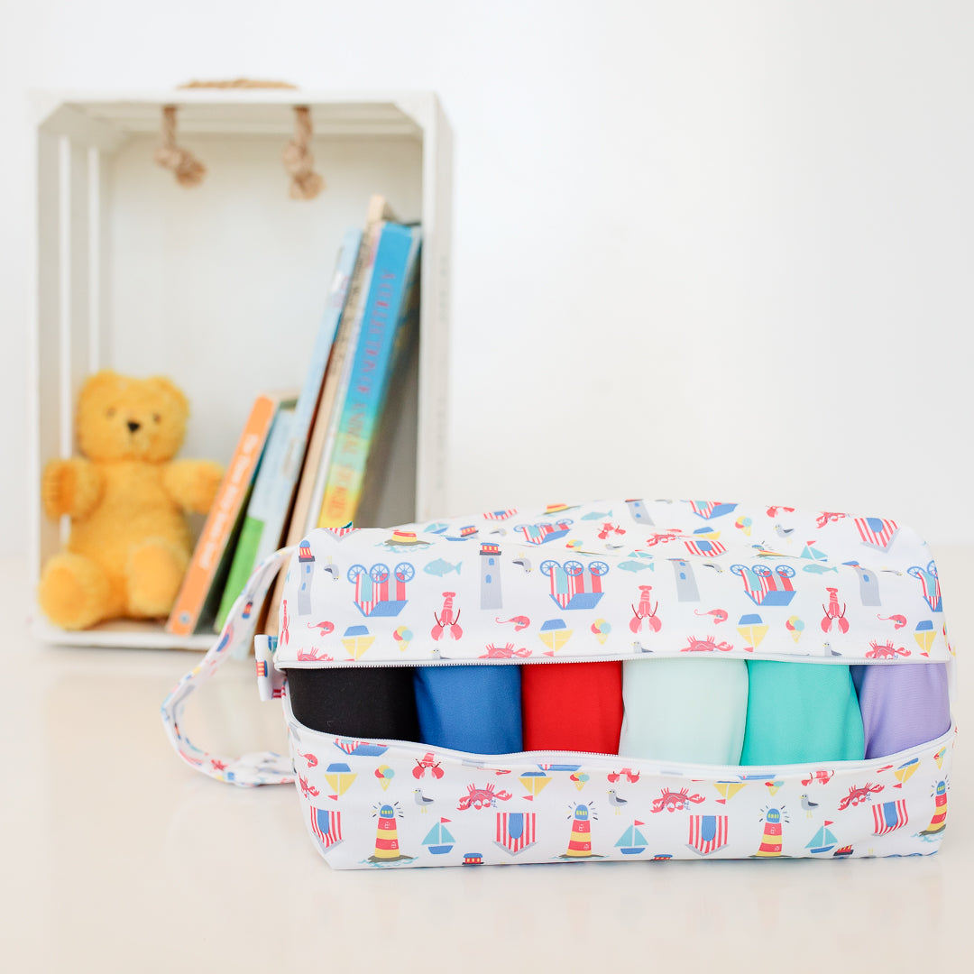 A Bubblebubs pod wet bag with six candie cloth nappies of different colours in front of some kid's toys.