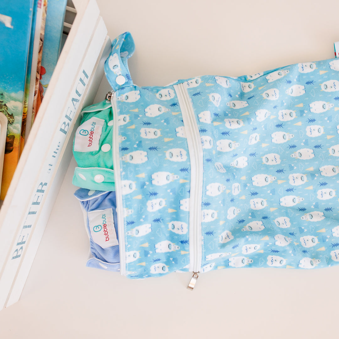 A Bubblebubs double pocket wet bag with some candie cloth nappies inside next to a box of books.