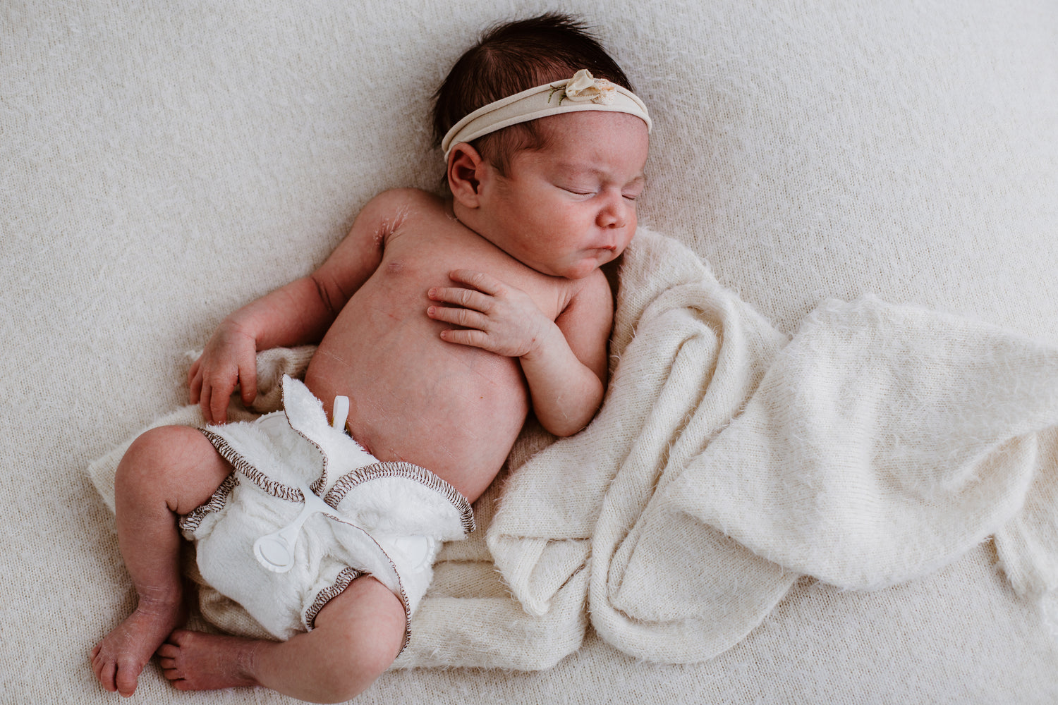 Sleeping baby waring a sweet band and a Bubblebubs Bambam cloth nappy with a snappi on a blanket cloud dreaming of dinner time.